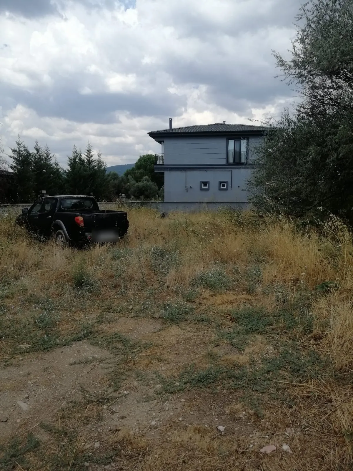 Menteşe Ortaköy'de yola cepheli 502 m² imarlı konut arsası — arka planda komşu iki katlı konutlar